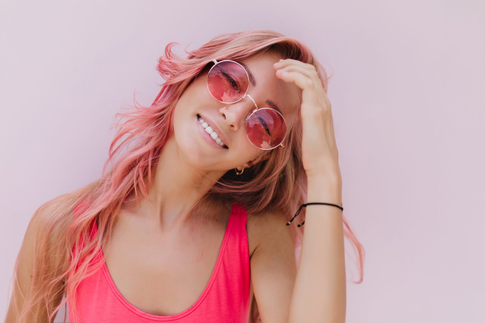 Close-up portrait of lady in pink crop top and sunglasses. Smiling long-haired young woman with casual hairstyle posing on white background.